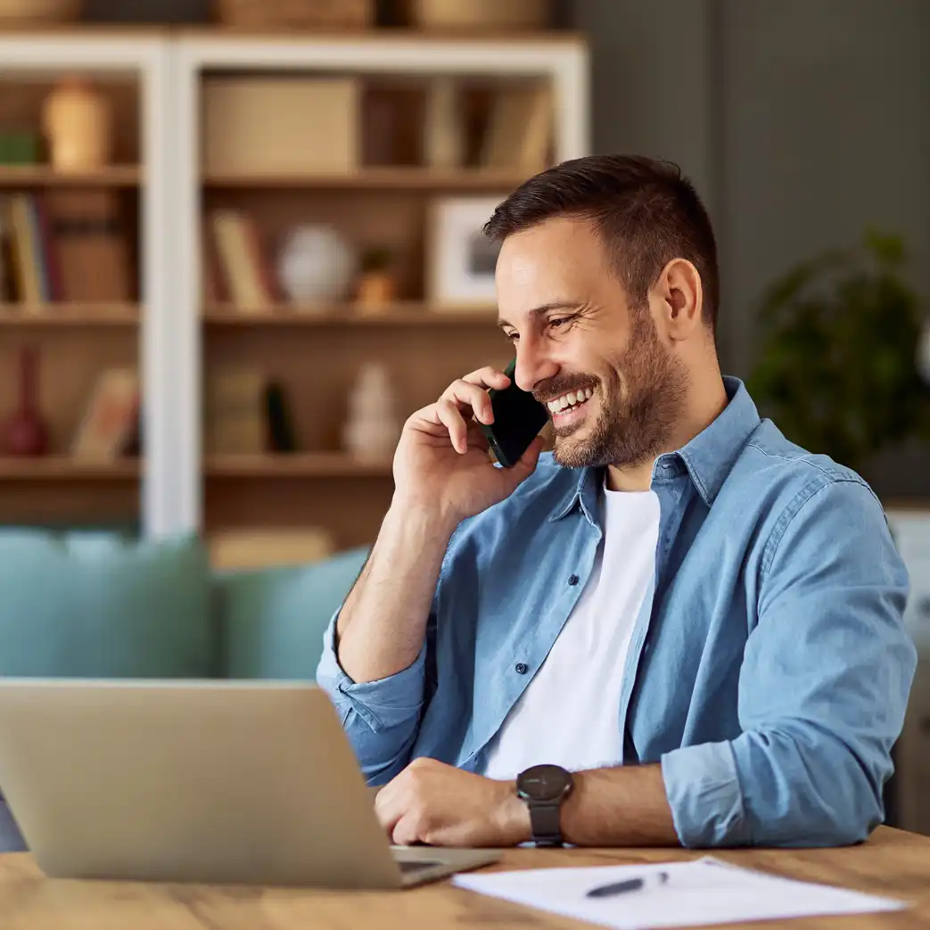 Man talking on the phone smiling while looking at his laptop