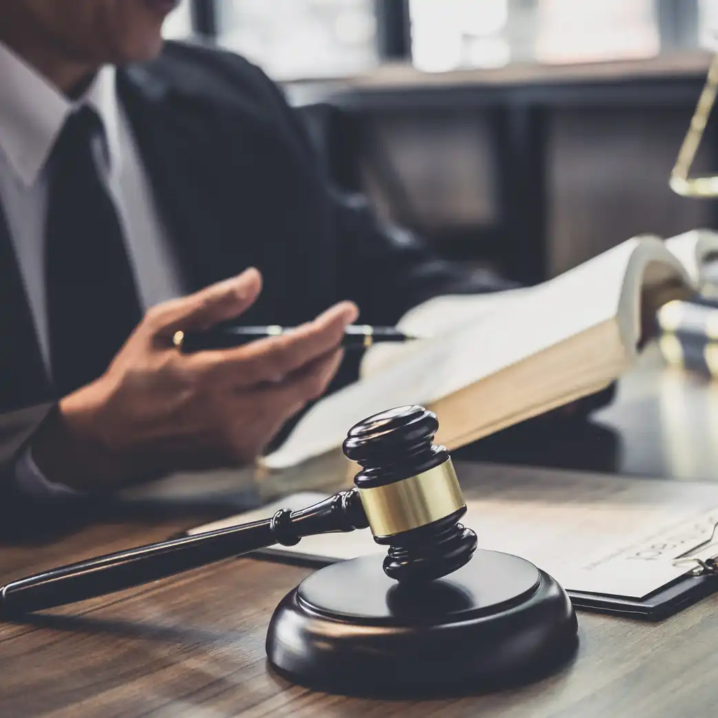 Lawyer holding an open book with a pencil in his other hand. Pictured on his desk is a clipboard with paper on it and a gavel that is propped up.