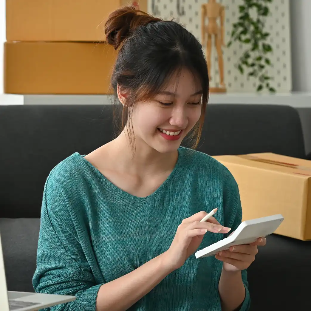 A woman smiling while using a calculator and holding a pencil in her hand simultaneously.