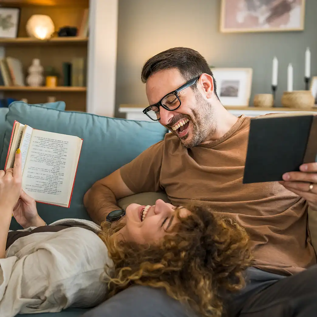 A woman is laying her head on a man's lap while they are both laughing and holding books.