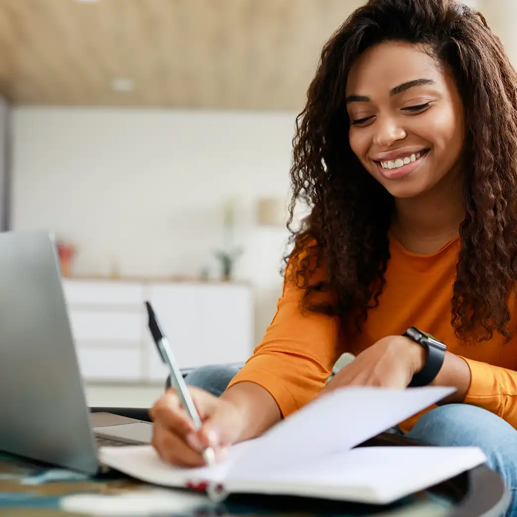 A woman smiling and writing something down in a journal.